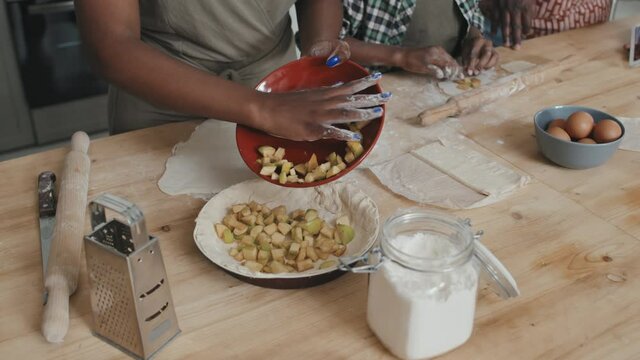 High-angle midsection shot with slowmo of unrecognizable African American woman making delicious apple pie while her husband and son helping her standing together by kitchen table