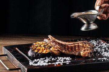 Pouring grilled beef steak with pepper sauce from a saucer