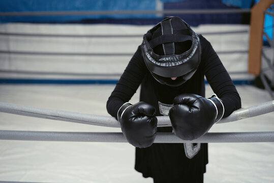 Relaxed Tired Exhausted Female Boxer Lying On The Ropes Of Ring. Woman In Hijab Rest After Hard Training.