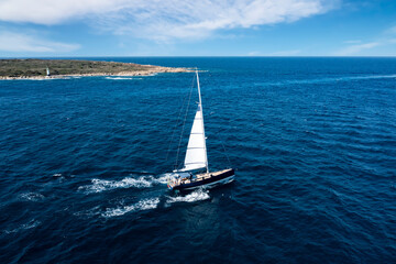 View from above, stunning aerial view of a sailboat sailing on a blue water during a sunny day. Costa Smeralda, Sardinia, Italy..