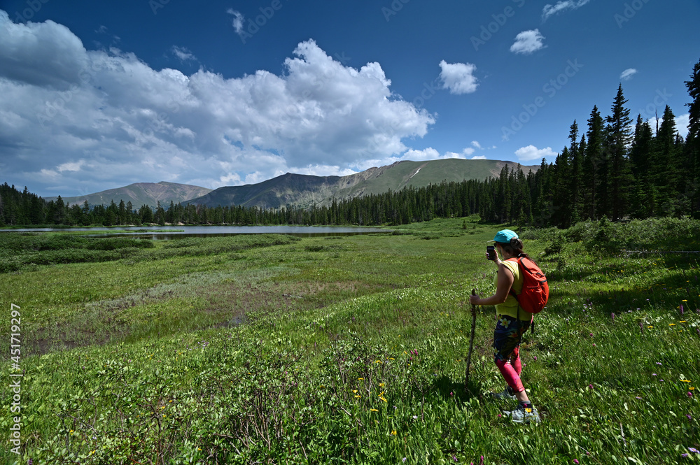 Wall mural Young female hiker photographs Hassell Lake in Arapaho National Forest, Colorado on sunny summer afternoon.