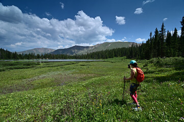 Young female hiker photographs Hassell Lake in Arapaho National Forest, Colorado on sunny summer afternoon.