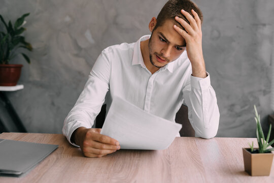 Worker or businessman with sick headache reads contract or bankruptcy documents. Manager consultant recruiting at work. Stress and depression of office workers. Business and work concept.