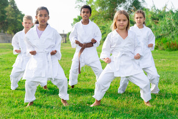 Naklejka na ściany i meble Kids in kimono doing kata moves during outdoor karate training.