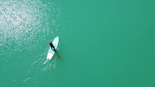 Drone footage of a girl floating in turquoise water. A woman uses a SUP board and paddle. Aerial top view