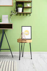 Table with stylish picture and decor near color wall
