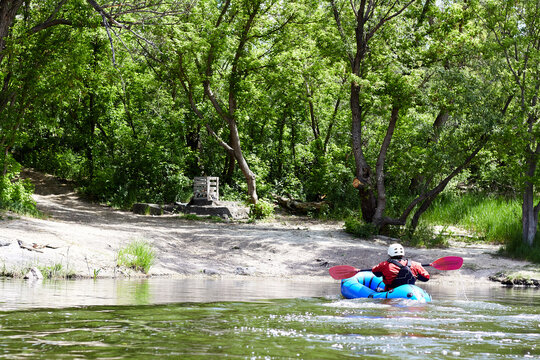Man paddling an inflatable blue packraft on a river in early spring spring
