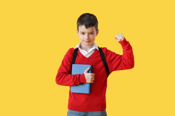 Little schoolboy with book on color background