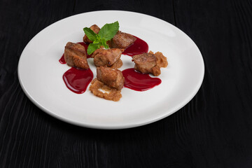 Delicacy Fried pork meat with zucchini puree and berries sauce decorated with mint on white plate on black wooden background