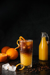 Glass of tasty coffee with orange juice on dark background