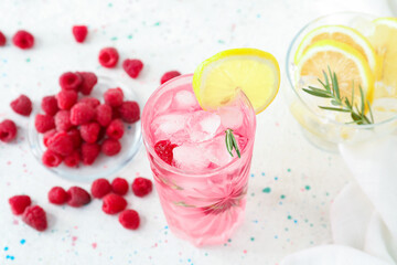 Glass of tasty raspberry lemonade and berries on light background