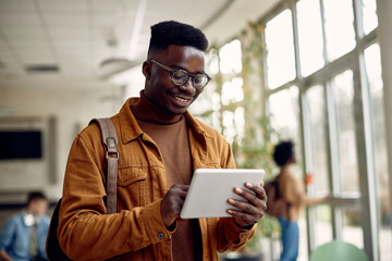 Fototapeta Happy African American student uses digital tablet at university hallway. obraz