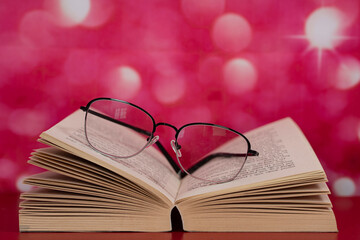 An open book with glasses on top of the pages. Selective focus points. Blurred background