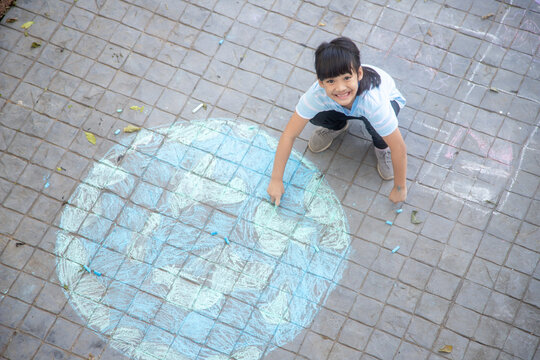 Asian children play outdoors. Child girl draws a planet globe with a map of the world colored chalk on the pavement, asphalt. Earth, peace day concert.