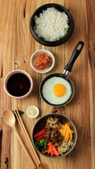 Top View Bibimbap Ingredients on Wooden Table, Rice, Saute Mix Vegetable, Mushroom, Beef Bulgogi, Bibimbap Spicy Sauce, Kimchi, and Sunny Side Egg.