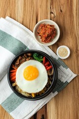 Bibimbap, Korean Spicy Salad with Rice and Sunny Side Fried Egg on Top, Traditionally Korean Mixed Rice Food Style. Top View on Wooden Table