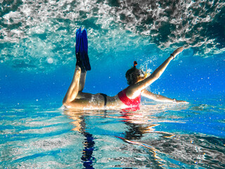 Free diver woman with white fins glides underwater with amazing sun rays. Freediving underwater in ocean