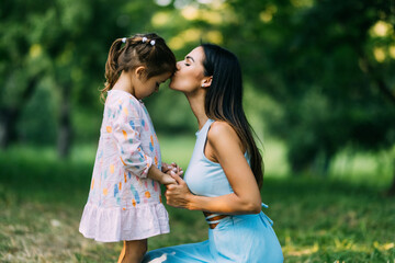 Naklejka premium Little girl kissing her mother in a green park