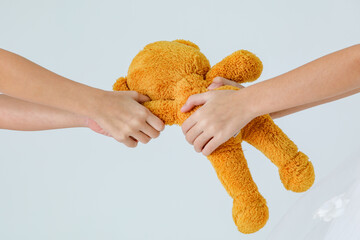 Close up studio shot of fluffy furry orange teddy bear doll was arms pulled by hands of two girl...