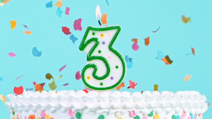 Colorful tasty birthday cake with candles shaped like the number 3. Pastel blue background.