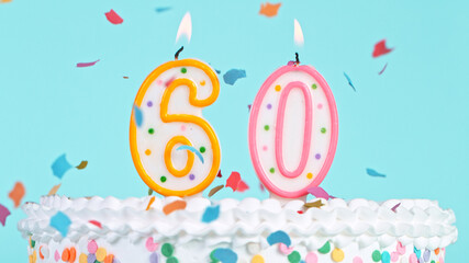 Colorful tasty birthday cake with candles shaped like the number 60. Pastel blue background.