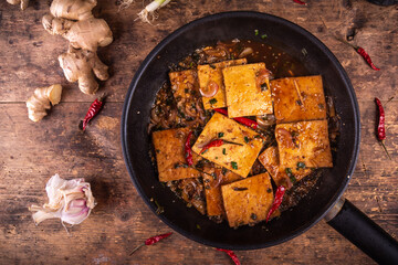 Stewed in hot sauce with peppers and onions tofu in a frying pan, top view on the table with ginger and garlic