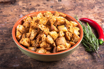 Fried croutons cooked with rosemary and hot pepper in a clay bowl on a rustic table, close-up