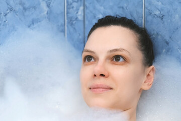 Portrait of young woman with closed eyes is relaxing lying in bath with foam at home after busy...