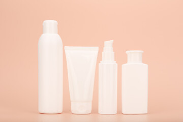 Set of white unbranded cosmetic bottles for face and body care in a row against pastel beige background. Concept of organic, natural, eco friendly cosmetics and beauty products for sensitive skin