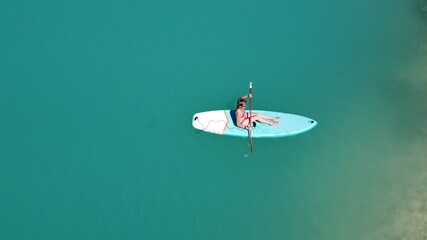 A girl in a dress floats on a glanders board on a pond with bright turquoise water. Warm summer day...