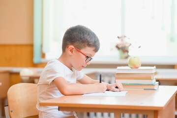 Elementary school boy at classroom desk trying to find new ideas for schoolwork.