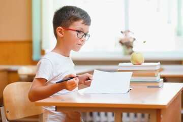 Elementary school boy at classroom desk trying to find new ideas for schoolwork. © Serhii