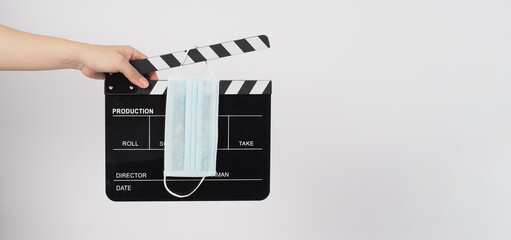 Hand is holding Clapper board or movie slate and face mask on white background.