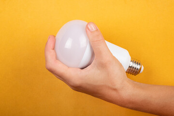 energy saving concept, led saving lamp in hand on yellow background.