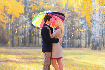 Portrait of happy loving young couple hugging with colorful umbrella in warm sunny day on yellow flying leaves background