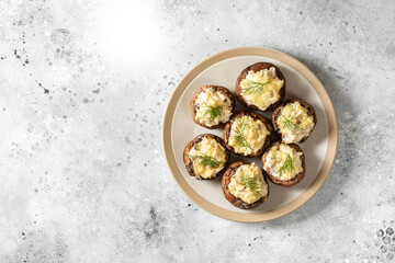 Stuffed mushroom champignons with cream cheese, chicken fillet and parmesan in a plate on the light gray kitchen table top view