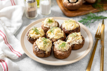 Stuffed mushroom champignons with cream cheese, chicken fillet and parmesan in a plate on the light gray kitchen table closeup