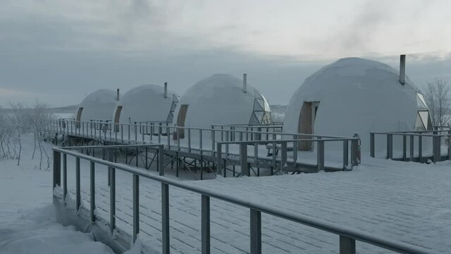 Row of igloo dome houses with glass panoramic windows standing on a wooden platform in glamping on a winter day