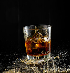 splash in glass with whiskey with ice on black background
