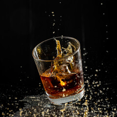 splash in glass with whiskey with ice on black background