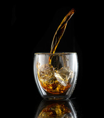 splash in double walled glass with whiskey with ice on black background