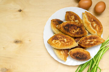 Fried pies with green onions and eggs on white plate, space for text