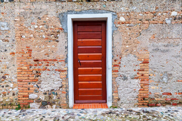 Fototapeta na wymiar Antica facciata con muro di mattoni e sasso ristrutturata con una porta di legno marrone chiusa. Antico mulino nel biotopo di Falmbro. 