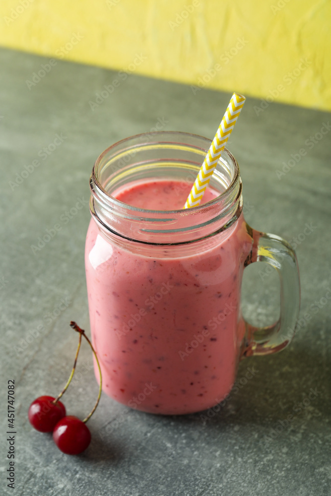 Wall mural Glass jar of cherry smoothie and ingredients on gray textured table