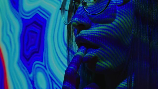A young woman puts a lsd acid blotter on her tongue. Multicolored psychedelic abstract background. The concept of psychedelia, nirvana and addiction