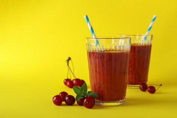 Glasses of cherry smoothie and ingredients on yellow background