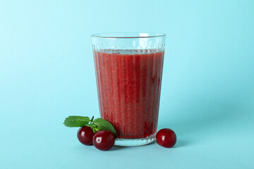 Glass of cherry smoothie and ingredients on blue background