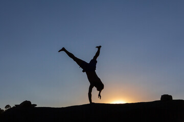 Boy doing acrobatics on a rock at sunset in autumn. Copy space. Backlight.
