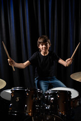 Fototapeta na wymiar The boy learns to play the drums in the studio on a black background. Music school student