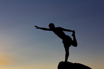 Silhouette of man practicing yoga at sunset on a rock in nature. Backlight. Copy space.